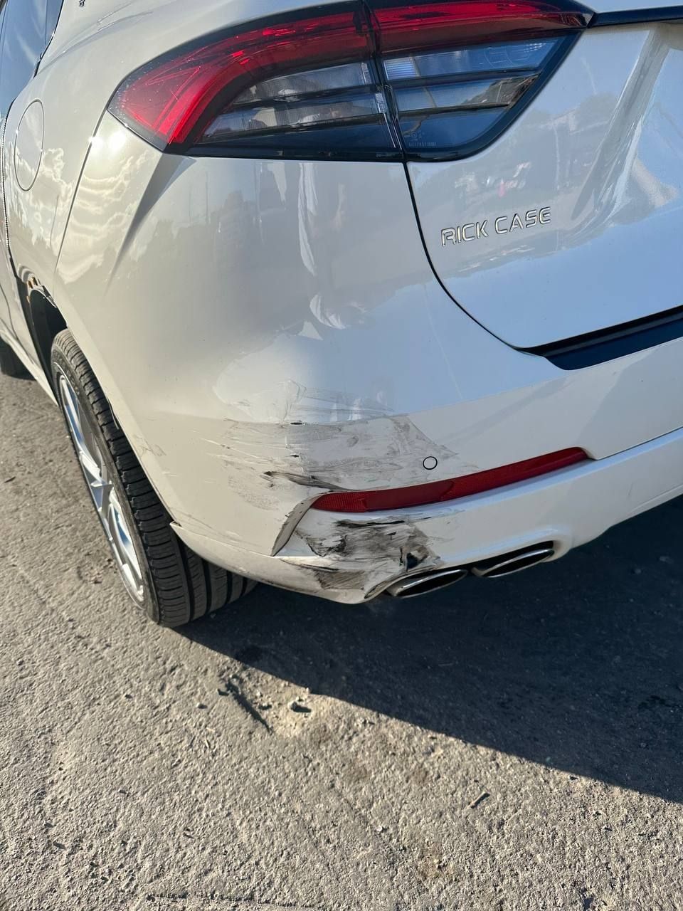 A white Maserati Levante with the rear bumper scraped and torn next to the exhaust
