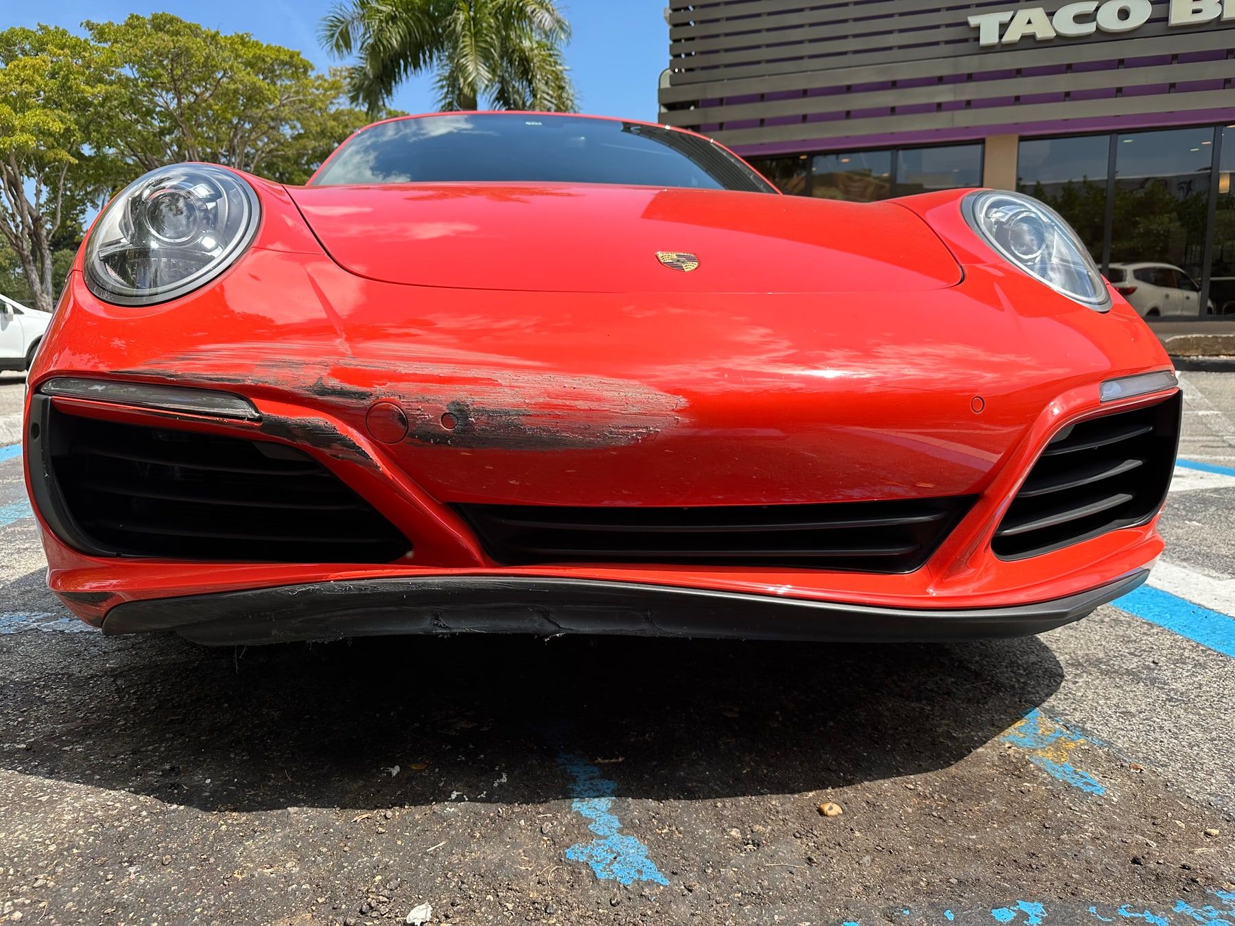 An orange Porsche 911 with a scraped, cracked front bumper
